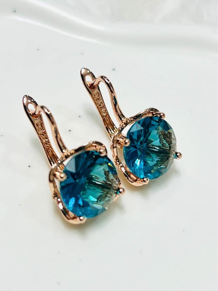 Top-down view of 14K rose gold London Blue Topaz earrings on a clean white surface.