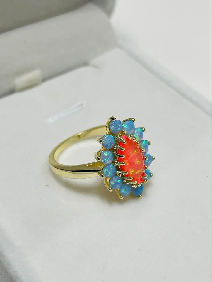  Side angle of a unique sterling silver ring with a marquise orange opal and a halo of blue opals.