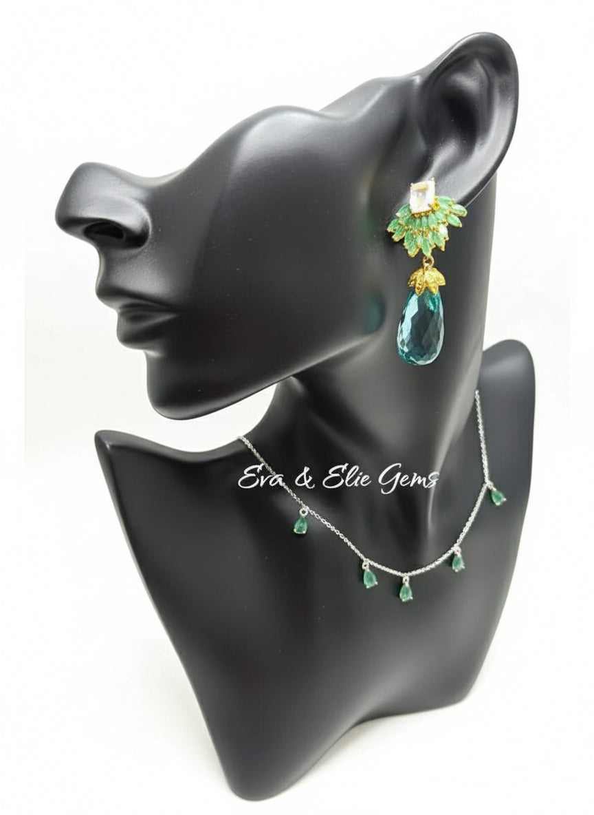 A mannequin wearing stunning drop earrings and necklace set. Features emerald, topaz, and aquamarine gemstones.