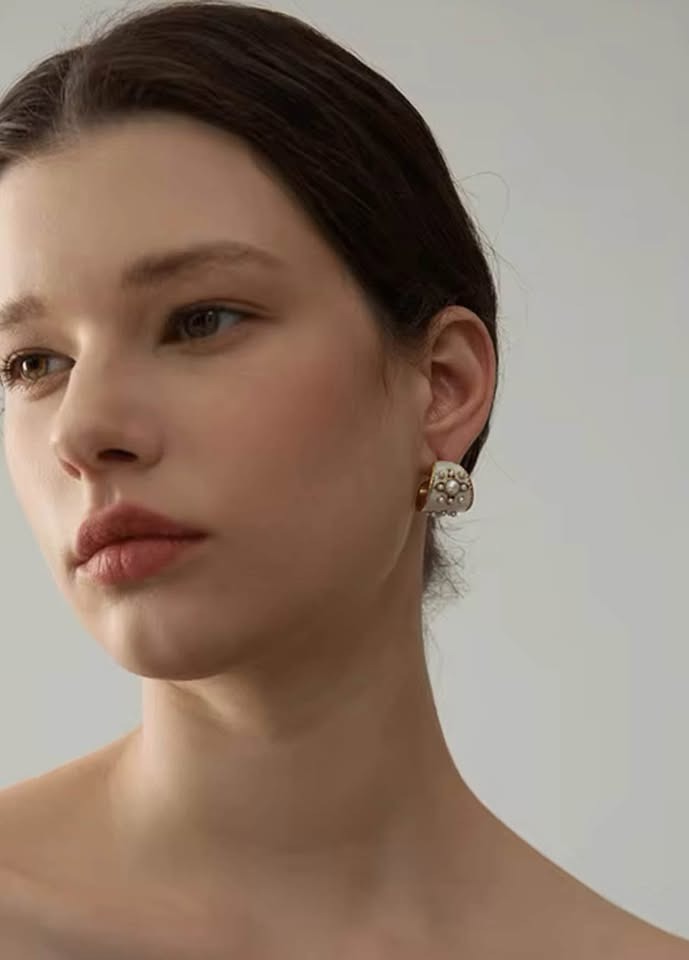 A woman modeling a vintage gold vermeil hoop earring with white enamel and pearls.