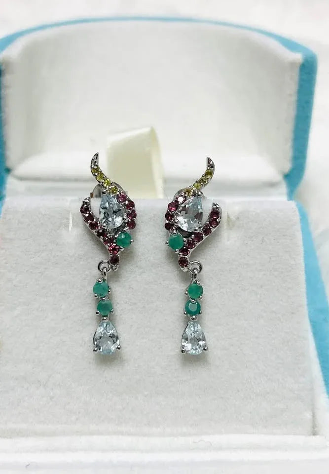 Close-up of elegant sterling silver drop earrings with natural aquamarine, emerald, and garnet.