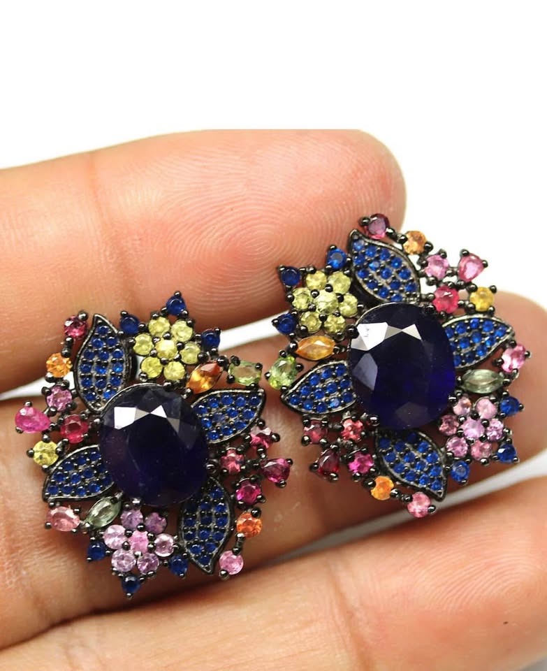 Handmade earrings with natural blue and colored sapphires in a vibrant floral design, held in a hand.