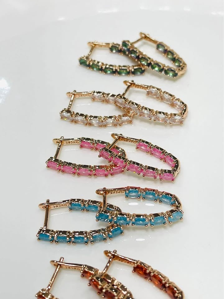 Angled view of a collection of multi-colored V-shaped inside-out tourmaline hoops in pink, blue, green, and clear.