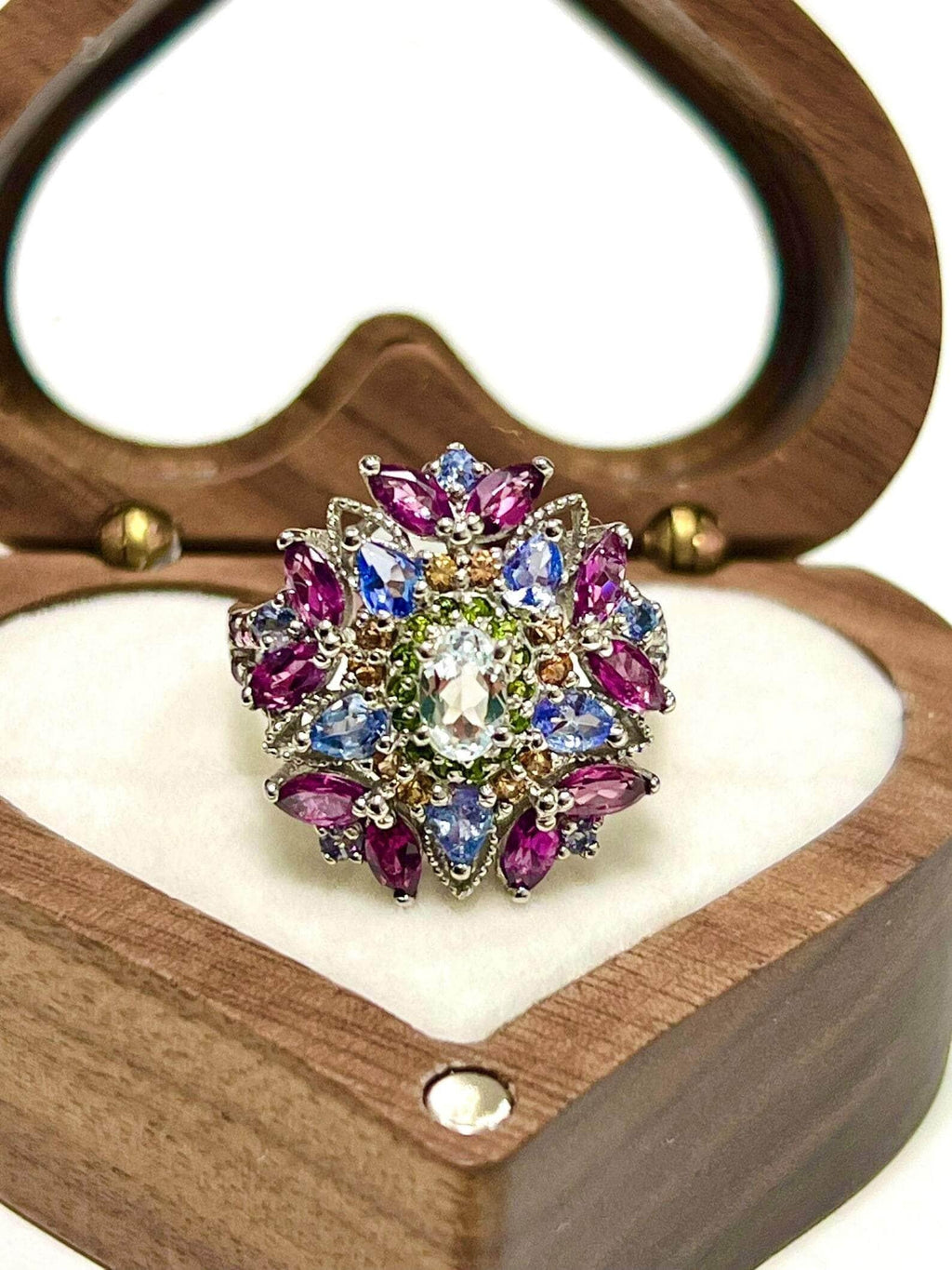 Exquisite floral ring with aquamarine, garnet, and tanzanite gemstones in a heart-shaped wooden box.