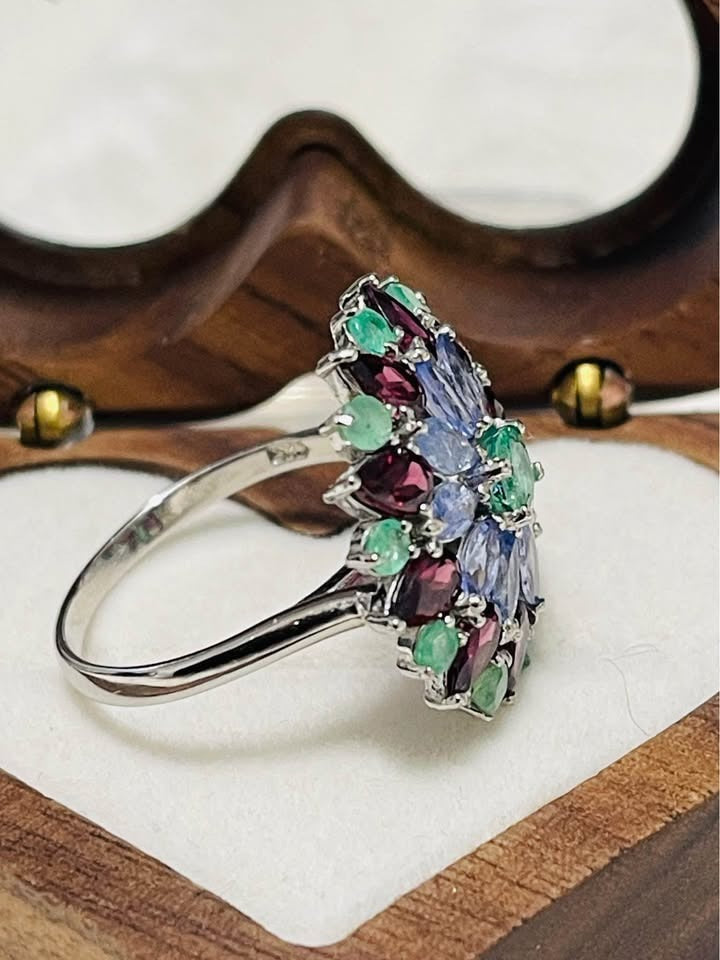  A vibrant floral cluster ring. This unique piece showcases the beautiful colors of tanzanite, emerald, and rhodolite garnet.
