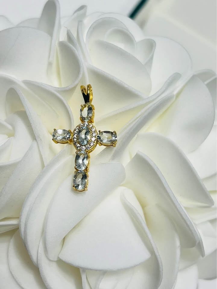 A close-up of a natural blue aquamarine cross pendant, highlighting the oval and round cut gemstones.