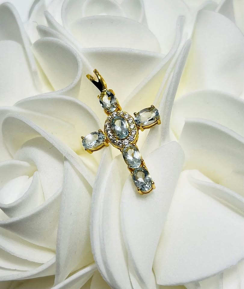 A natural aquamarine cross pendant with a halo of small white stones on a beautiful white floral background.
