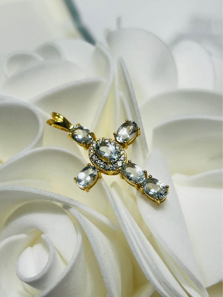 A stunning natural blue aquamarine cross pendant, displayed on a white floral background.