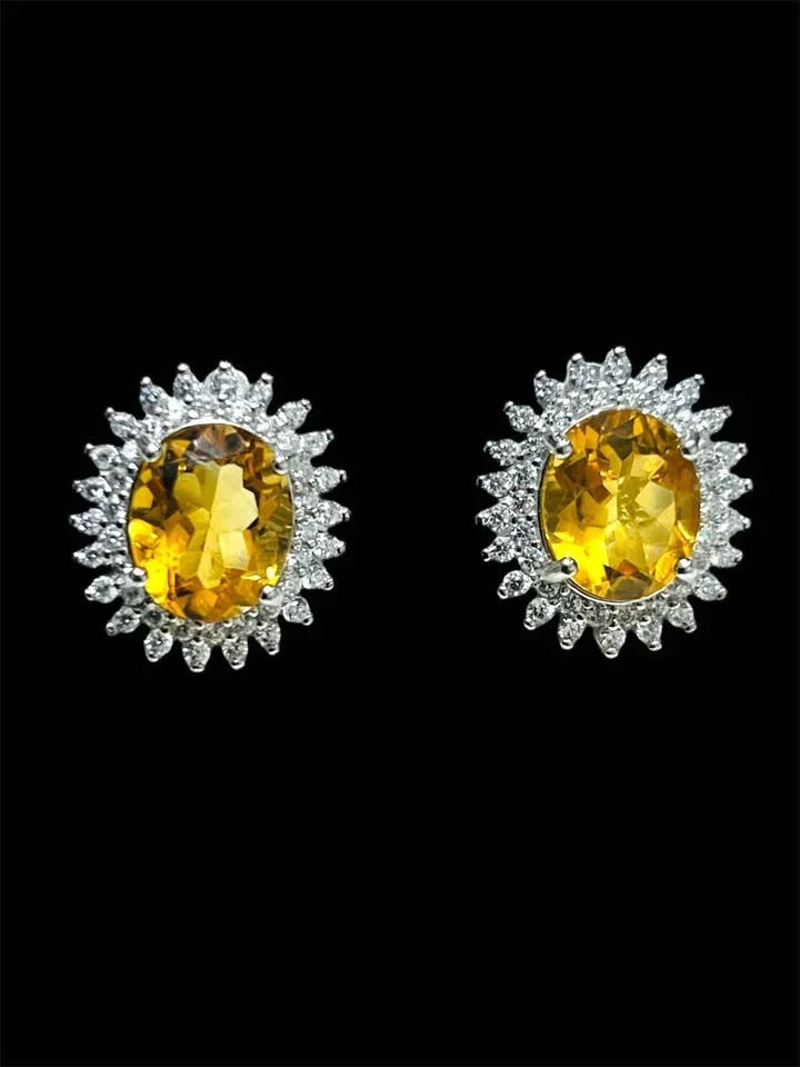 Pair of natural citrine oval halo earrings with brilliant white accents against a dark background.