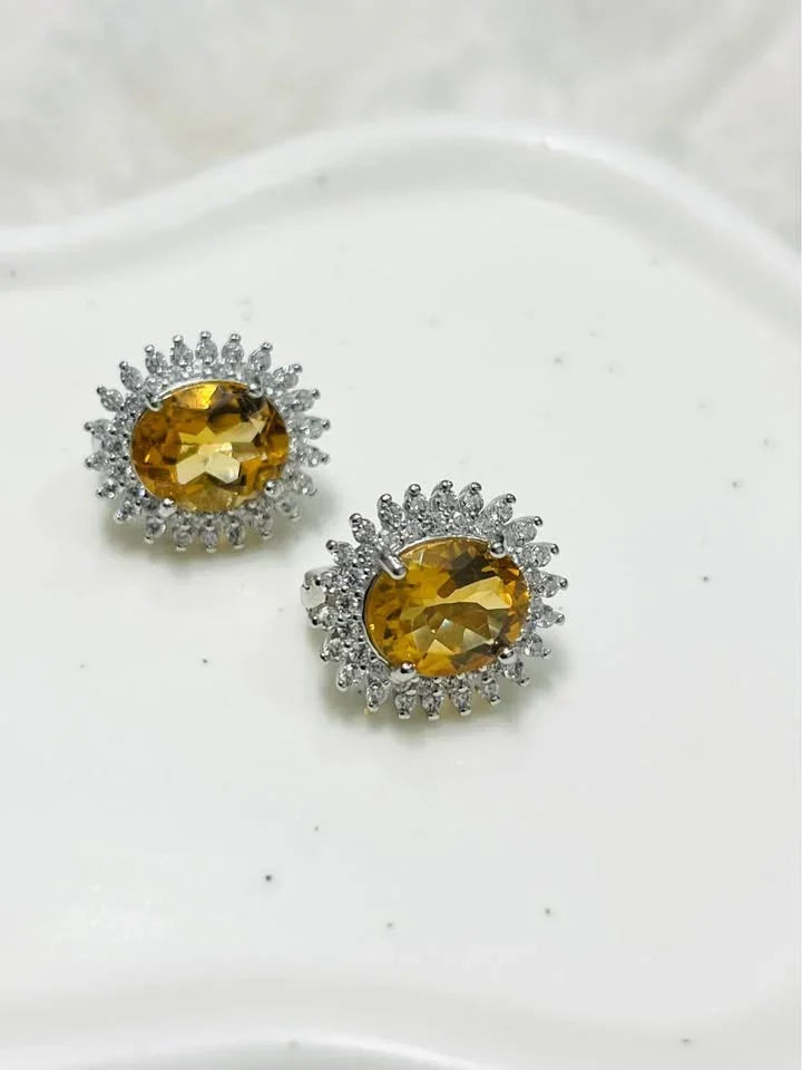 Angled view of natural citrine oval halo earrings, bright yellow gems, white background.