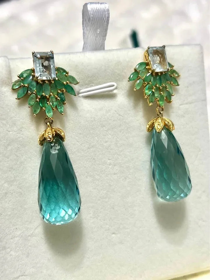  An elegant pair of drop earrings. The design features a cluster of emeralds with a central topaz and a large aquamarine.