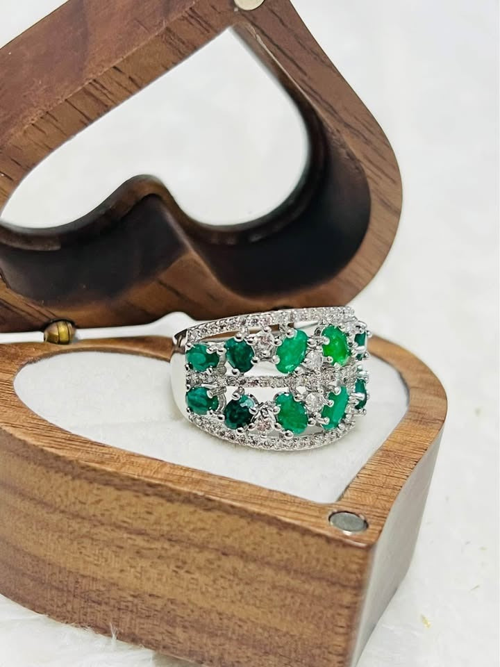 Top view of a striking sterling silver ring with vibrant natural emeralds, artfully displayed in an open heart-shaped box.