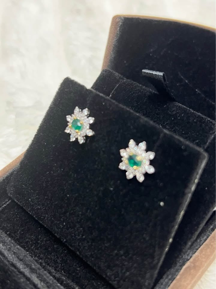 Angled view of natural emerald and white topaz flower stud earrings in a velvet-lined box.
