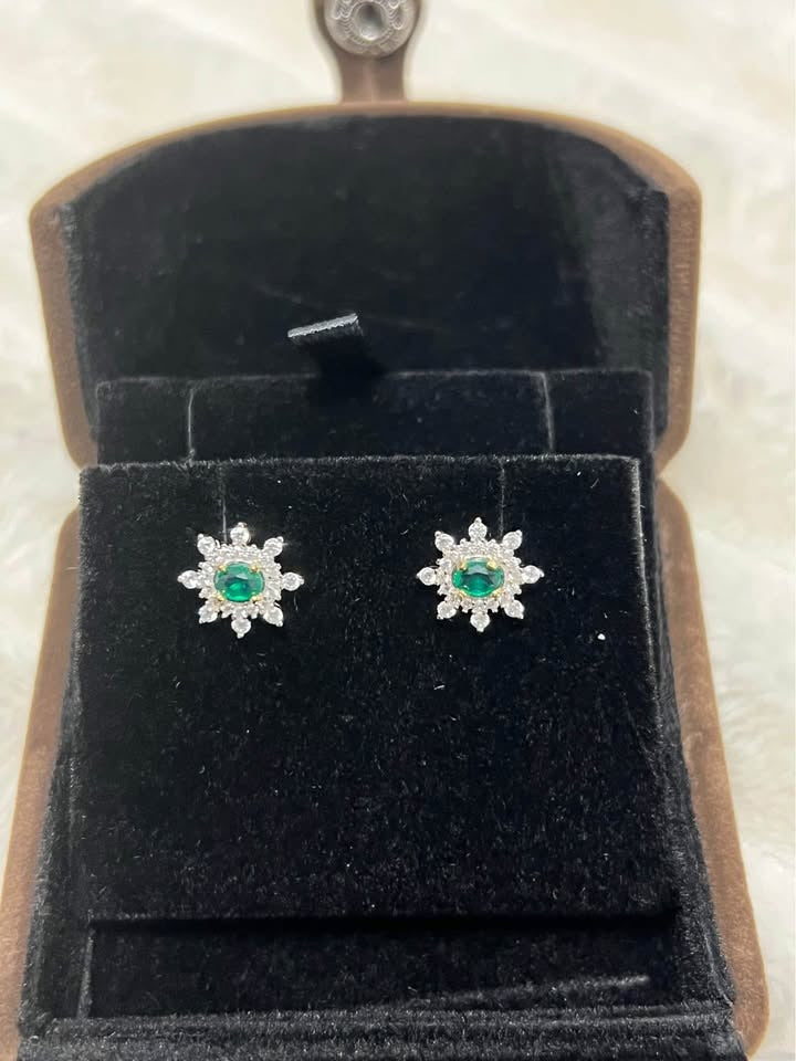 Top-down view of natural emerald and white topaz flower stud earrings in a brown velvet box.