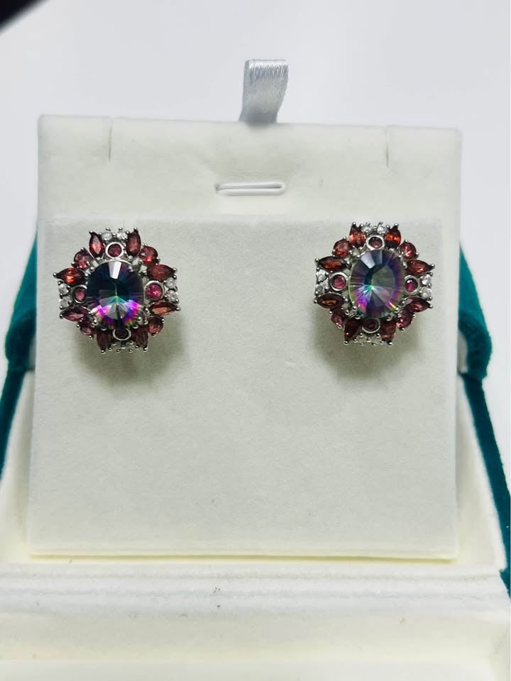 A top-down view of a pair of earrings featuring vibrant mystic quartz and deep red garnet stones.