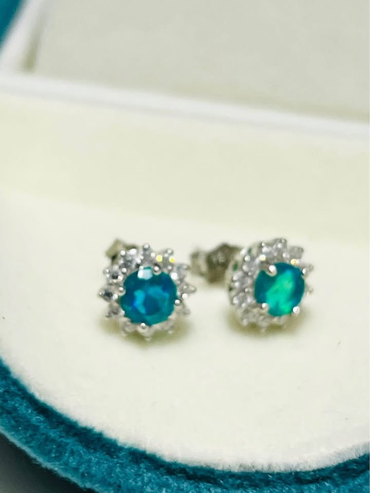 Close-up of natural silver stud earrings with shimmering blue fire opal stones, capturing their brilliant color.