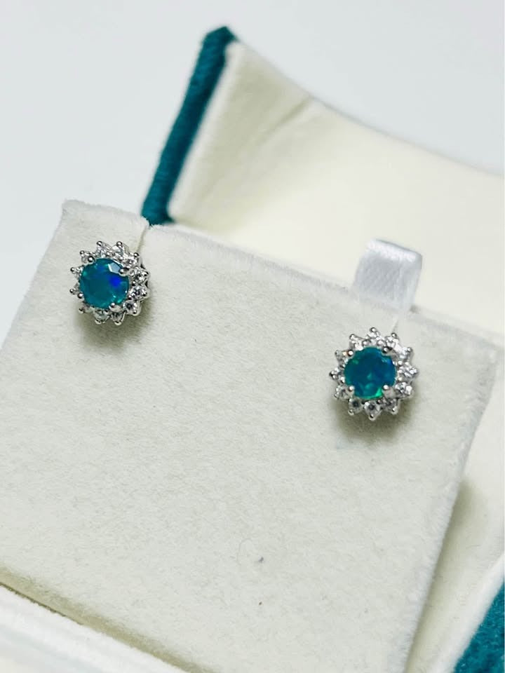 Natural silver stud earrings with vibrant blue fire opal and a halo of sparkling stones, displayed in a jewelry box