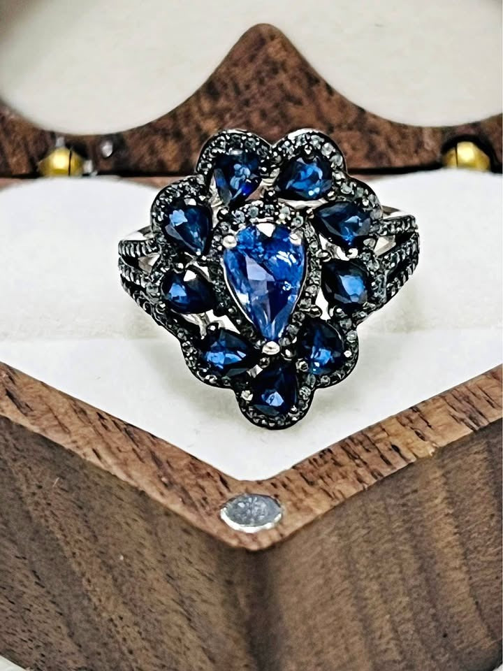  Close-up of a luxurious cocktail ring with a pear-cut tanzanite gemstone and deep blue sapphire accents.