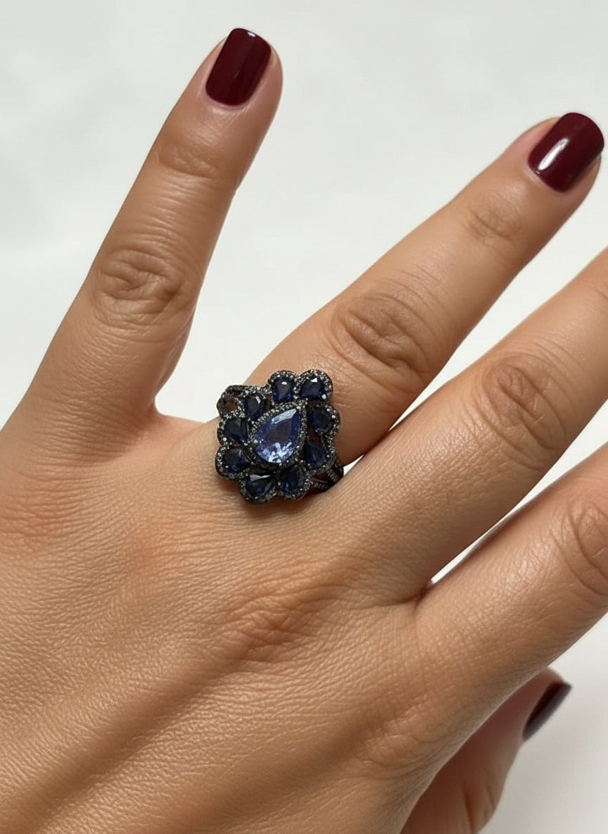 Stunning cocktail ring featuring a large natural tanzanite center stone and halo of blue sapphires on a hand.