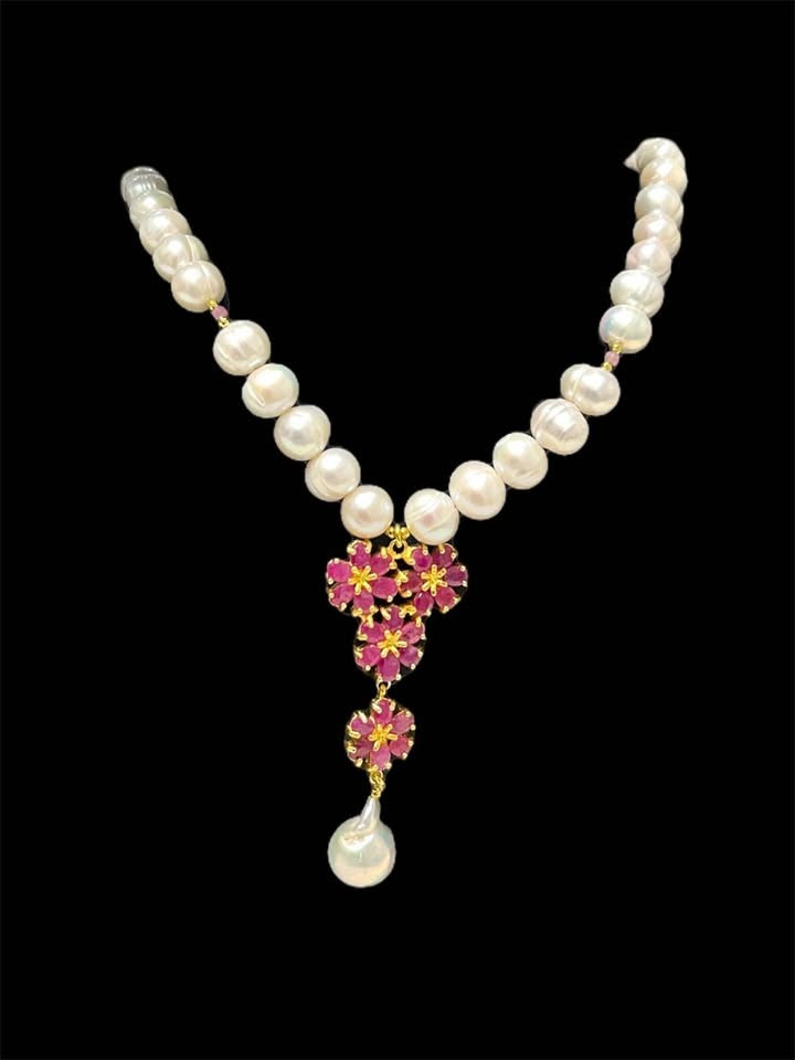 Elegant freshwater pearl necklace with a vibrant ruby flower cluster pendant on a black background.