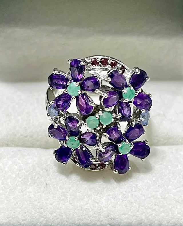 Bold sterling silver ring adorned with natural amethyst and emeralds in a vibrant floral pattern.