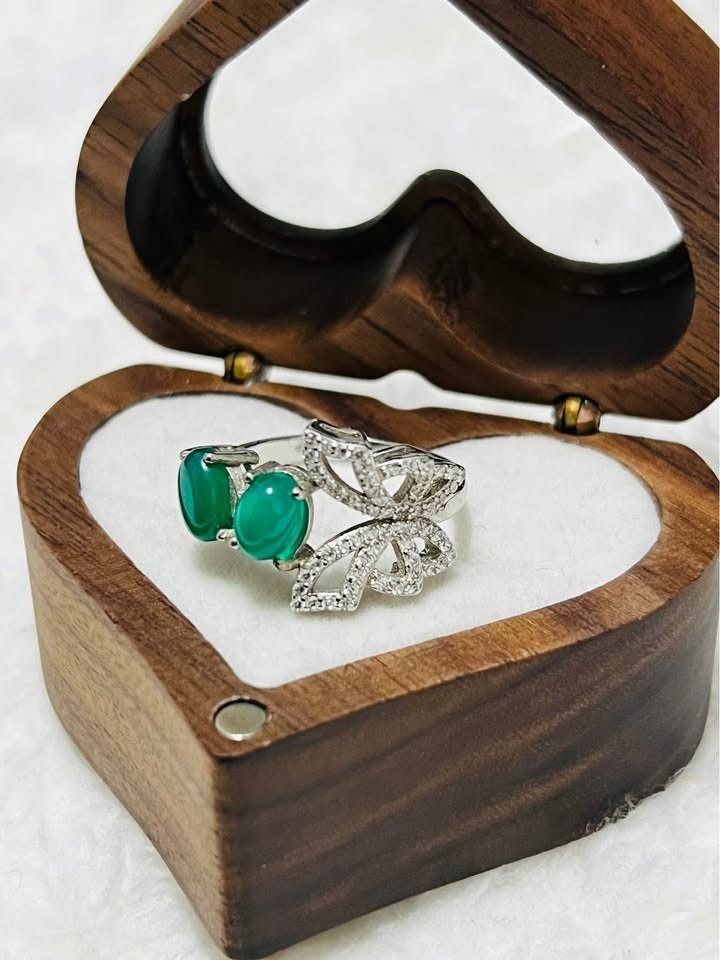Close-up of a nature-inspired sterling silver ring featuring natural emeralds and a diamond-studded butterfly, in a box.