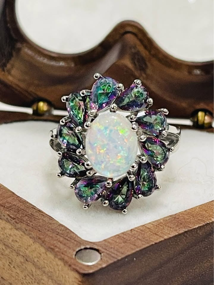 A detailed view of a ring with a fiery oval opal and iridescent mystic topaz halo, resting in a heart-shaped box.