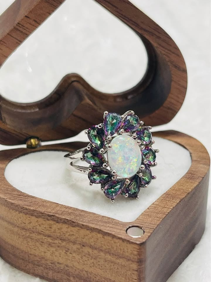 An angled shot of the opal and mystic topaz ring in a wooden heart-shaped box, against a white background.