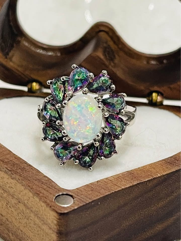 Close-up of a stunning ring with an oval opal center surrounded by pear-shaped mystic topaz stones in a heart box.