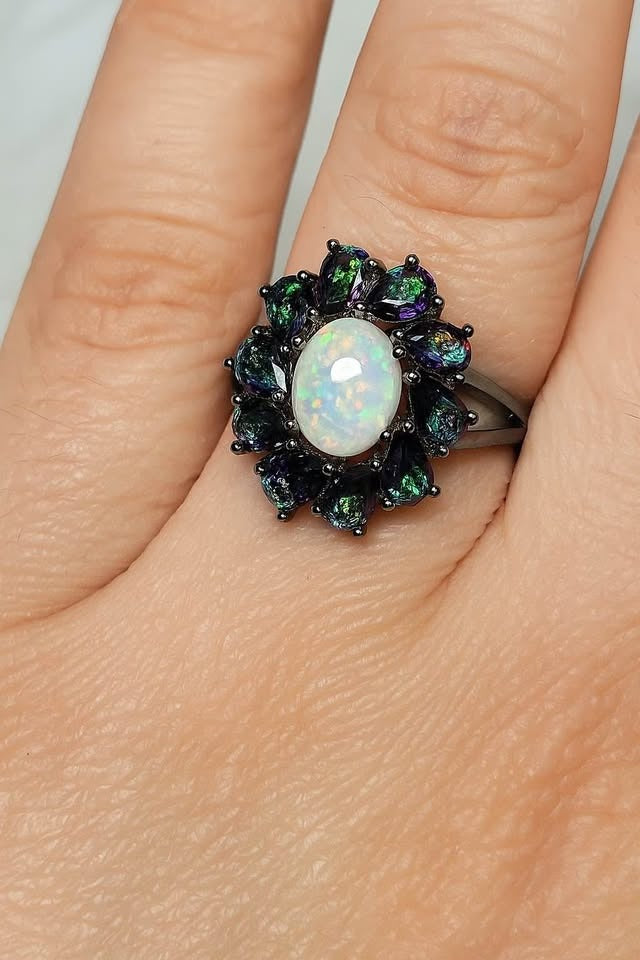 A beautiful opal and mystic topaz cluster ring worn on a finger, showcasing its intricate design and sparkle.