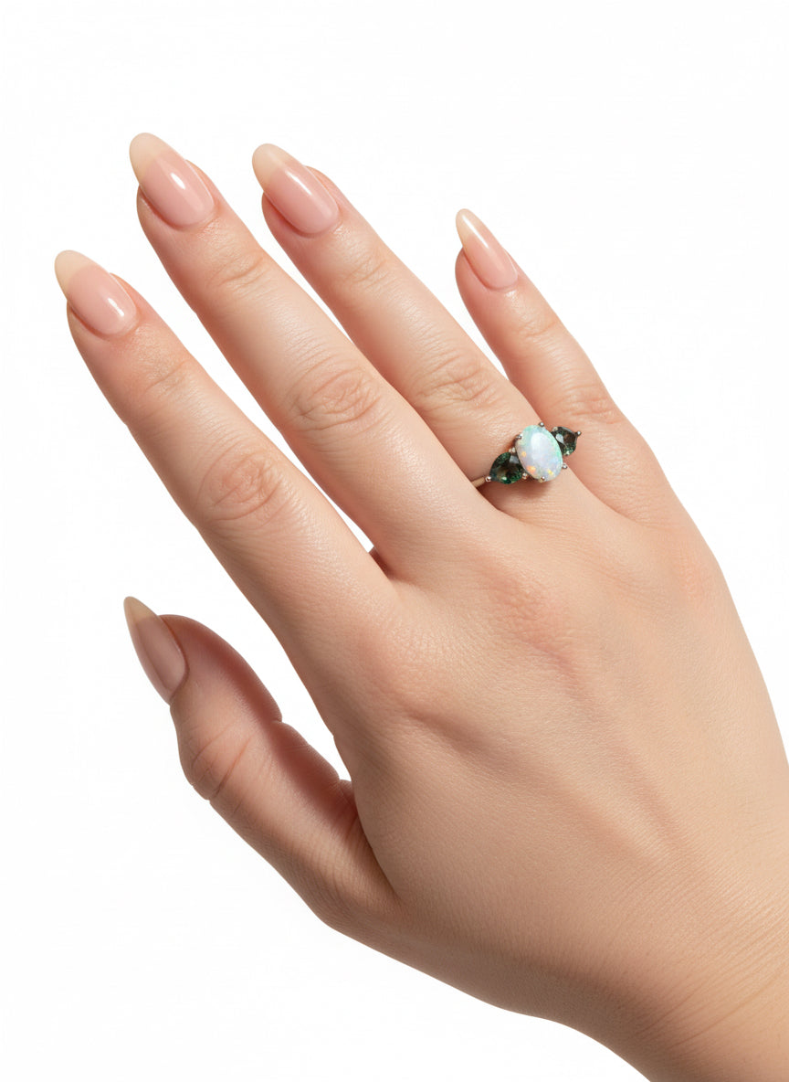 Hand with natural nails wearing a 14K gold-plated ring featuring an oval fire opal and two mystic topaz gems.