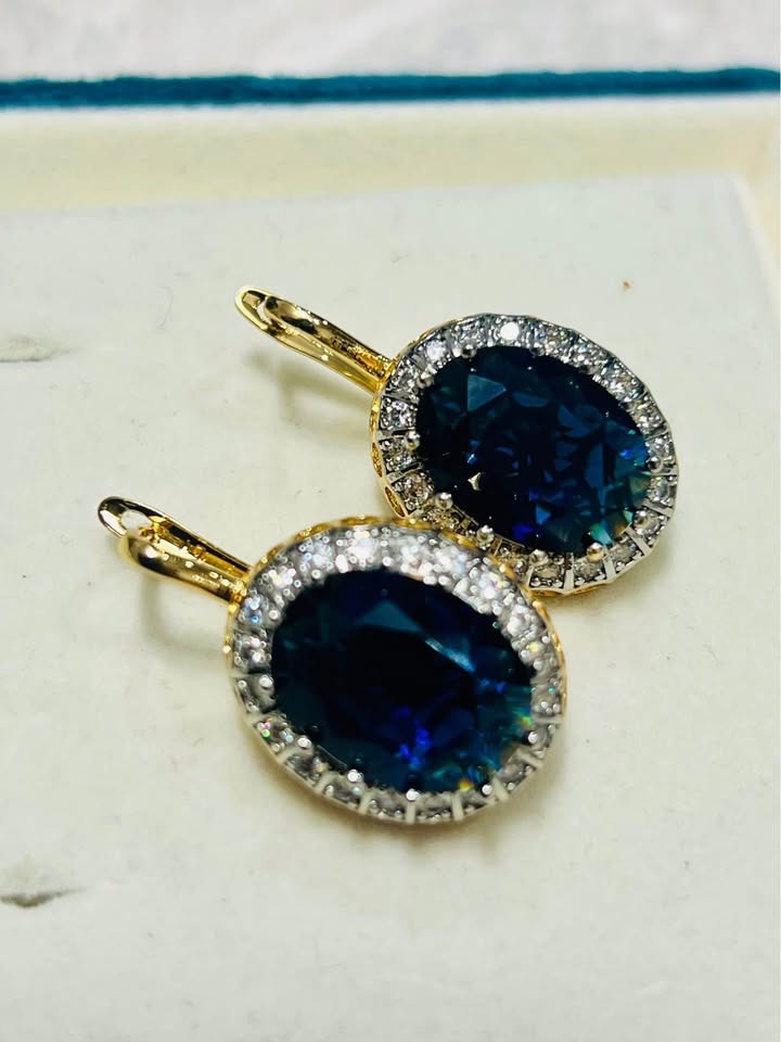 A pair of oval blue sapphire earrings, each encircled by a dazzling diamond halo in a gold setting.