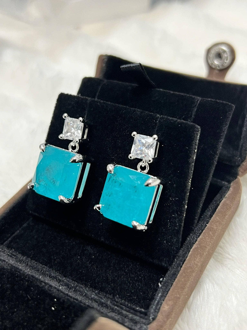 Angled view of striking emerald-cut Paraiba tourmaline earrings, showcasing their brilliant color and design.
