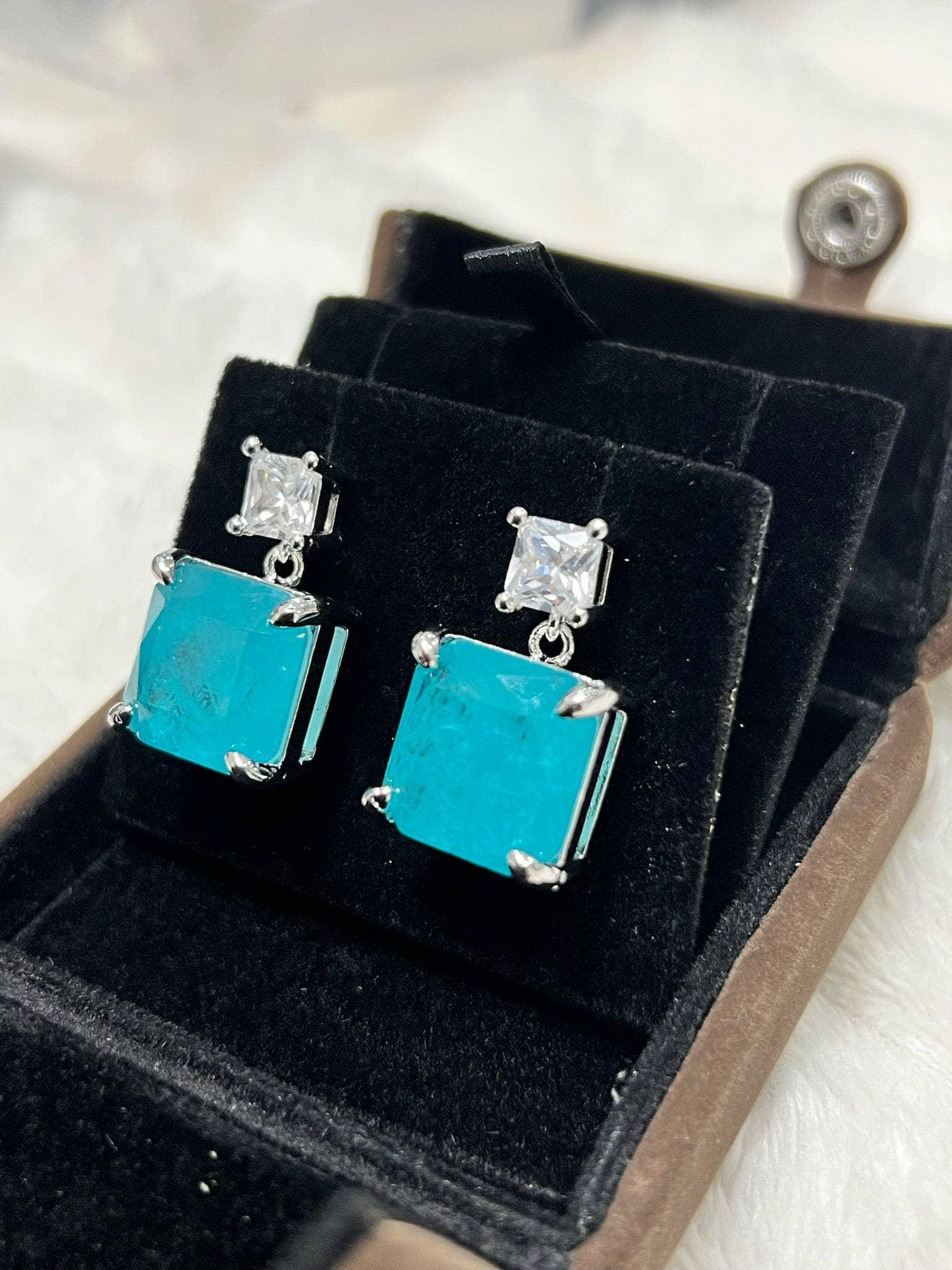 Angled view of striking emerald-cut Paraiba tourmaline earrings, showcasing their brilliant color and design.