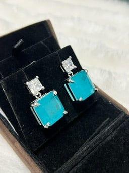 Stunning emerald-cut Paraiba tourmaline drop earrings, captured from a dynamic side angle in their display box.