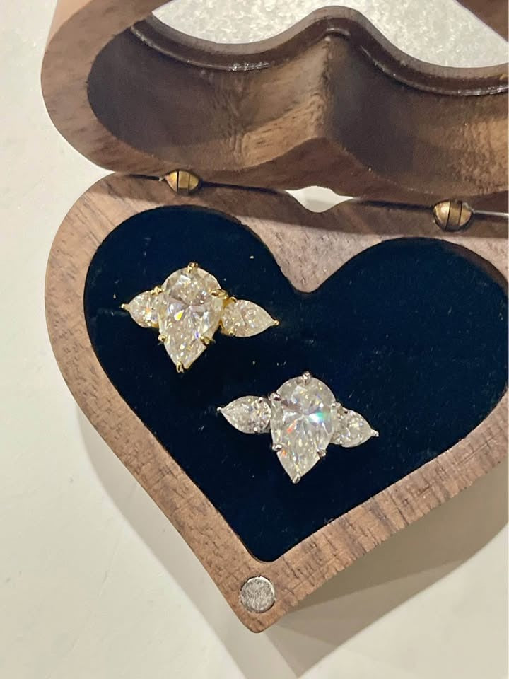 Two dazzling 4 carat pear-cut moissanite rings, one in gold and one in silver, nestled in a heart-shaped box.
