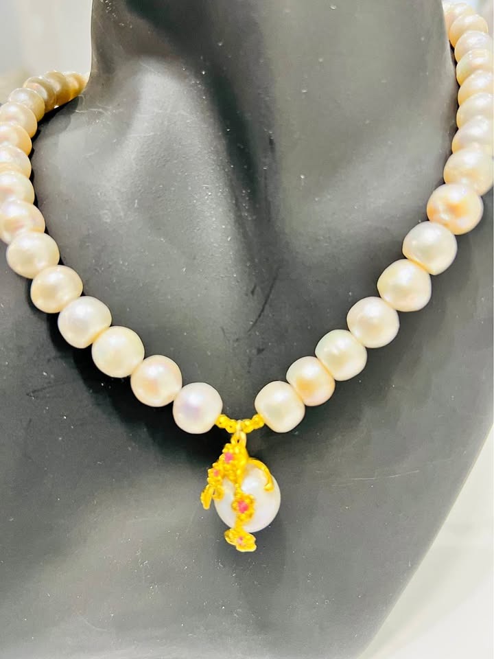 A natural pearl necklace with a unique gold pendant featuring a large pearl and pink ruby flowers.