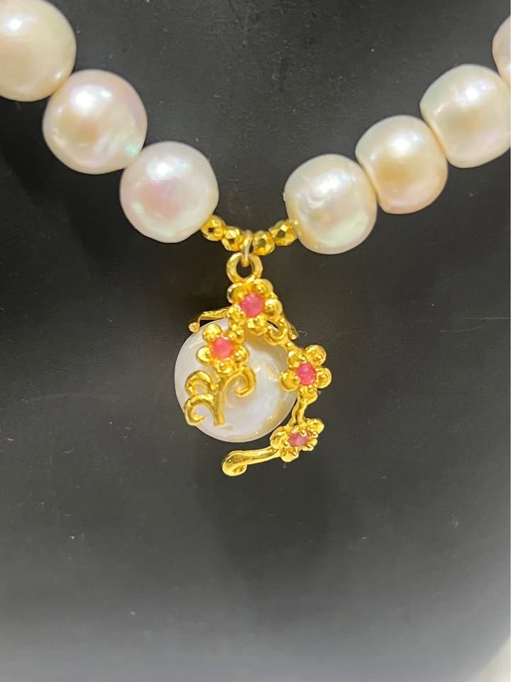 Close-up of a pearl pendant with a detailed gold flower design and vibrant pink ruby accents.