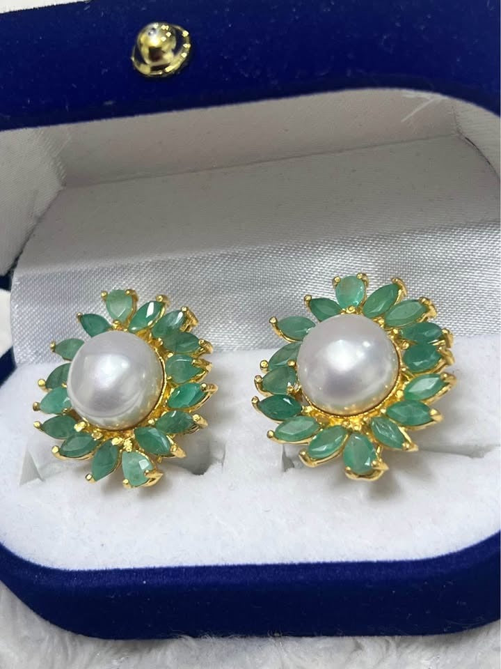  Close-up of natural South Sea pearl and emerald flower-design earrings in a blue velvet box.
