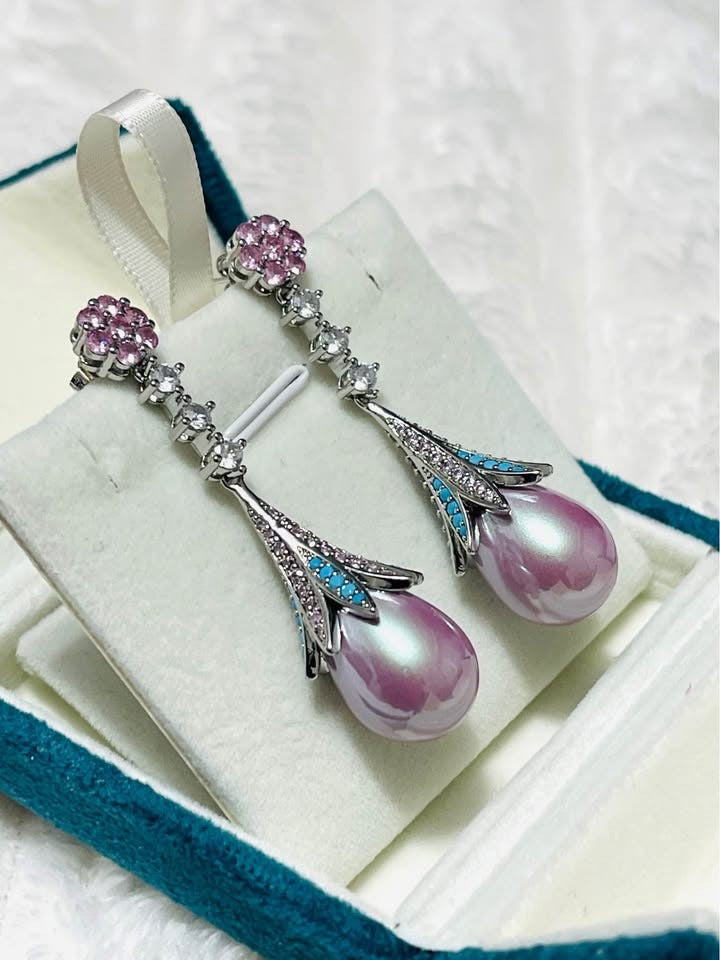 Close-up detail of pink pearl drop earrings featuring turquoise inlay and brilliant cubic zirconia stones.