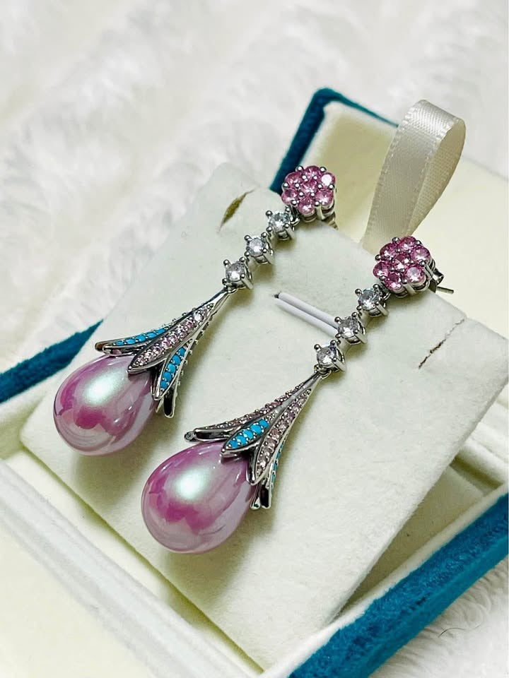 Angled view of long pink pearl and turquoise dangle earrings with sparkling pink and clear stones.