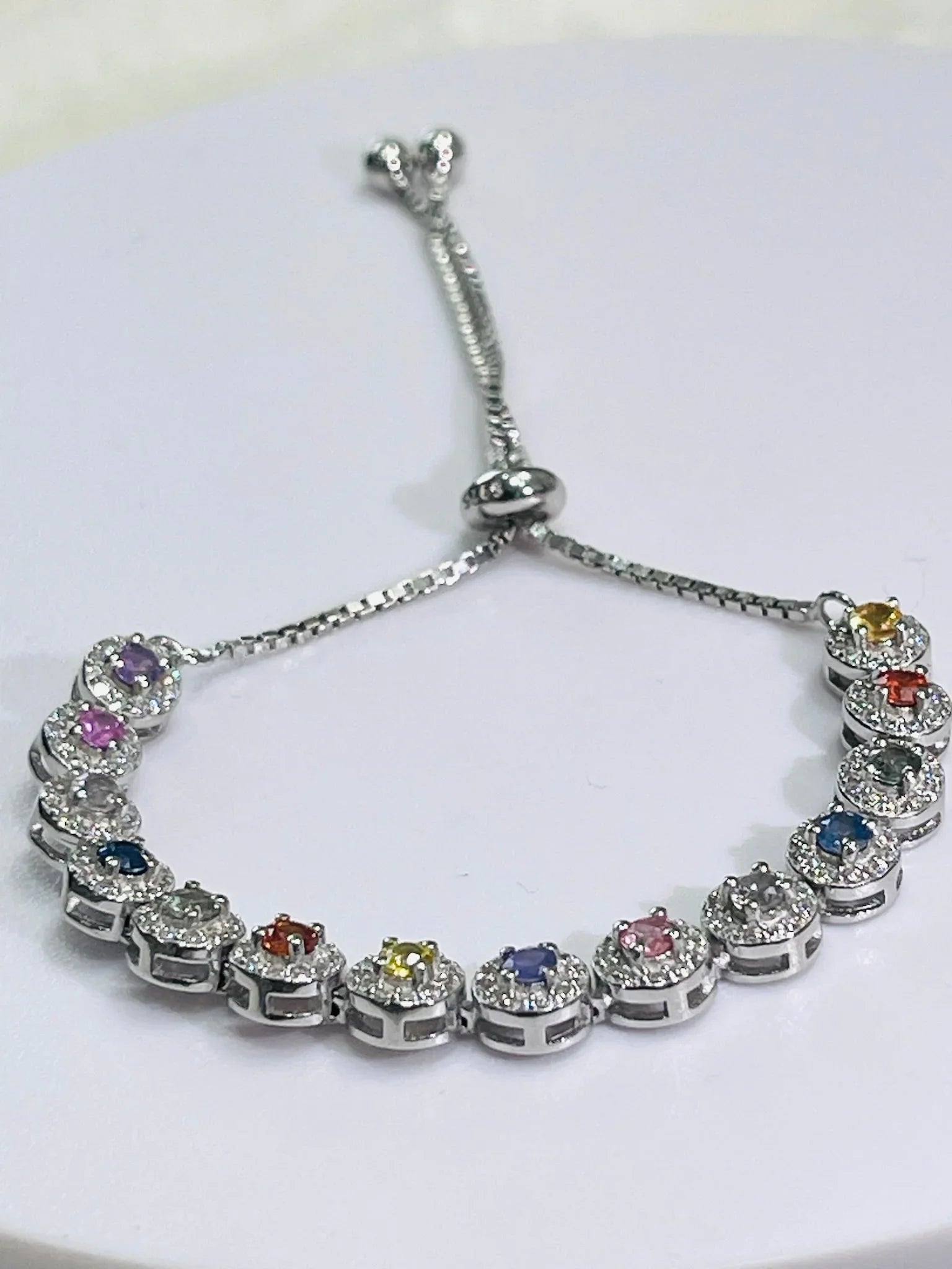 Angled view of a silver bolo bracelet with an array of vibrant, round gemstones, each set in a halo of clear stones.