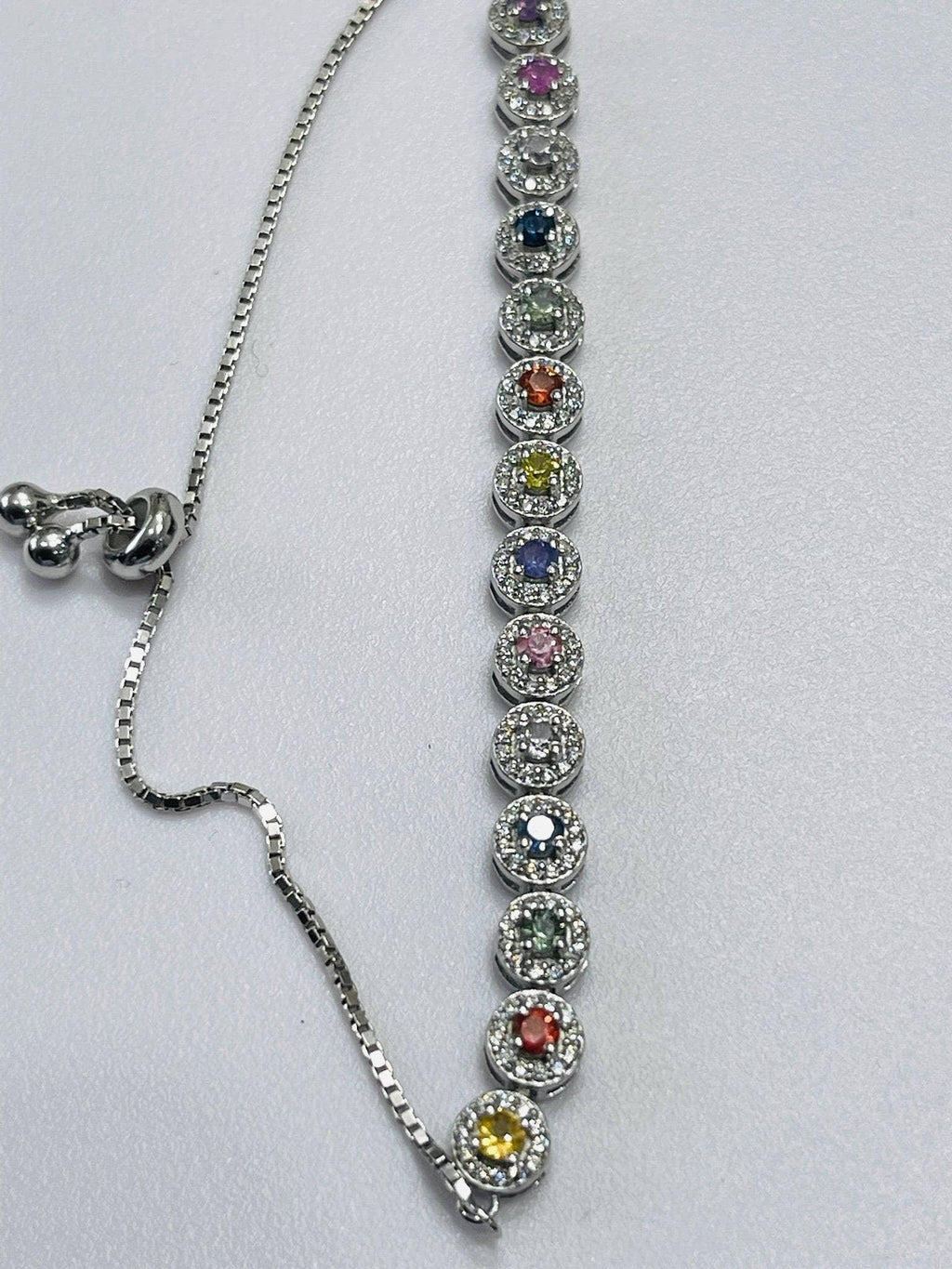  Close-up of a silver bolo bracelet showing multiple round, colorful gemstones in halos, with the adjustable chain.