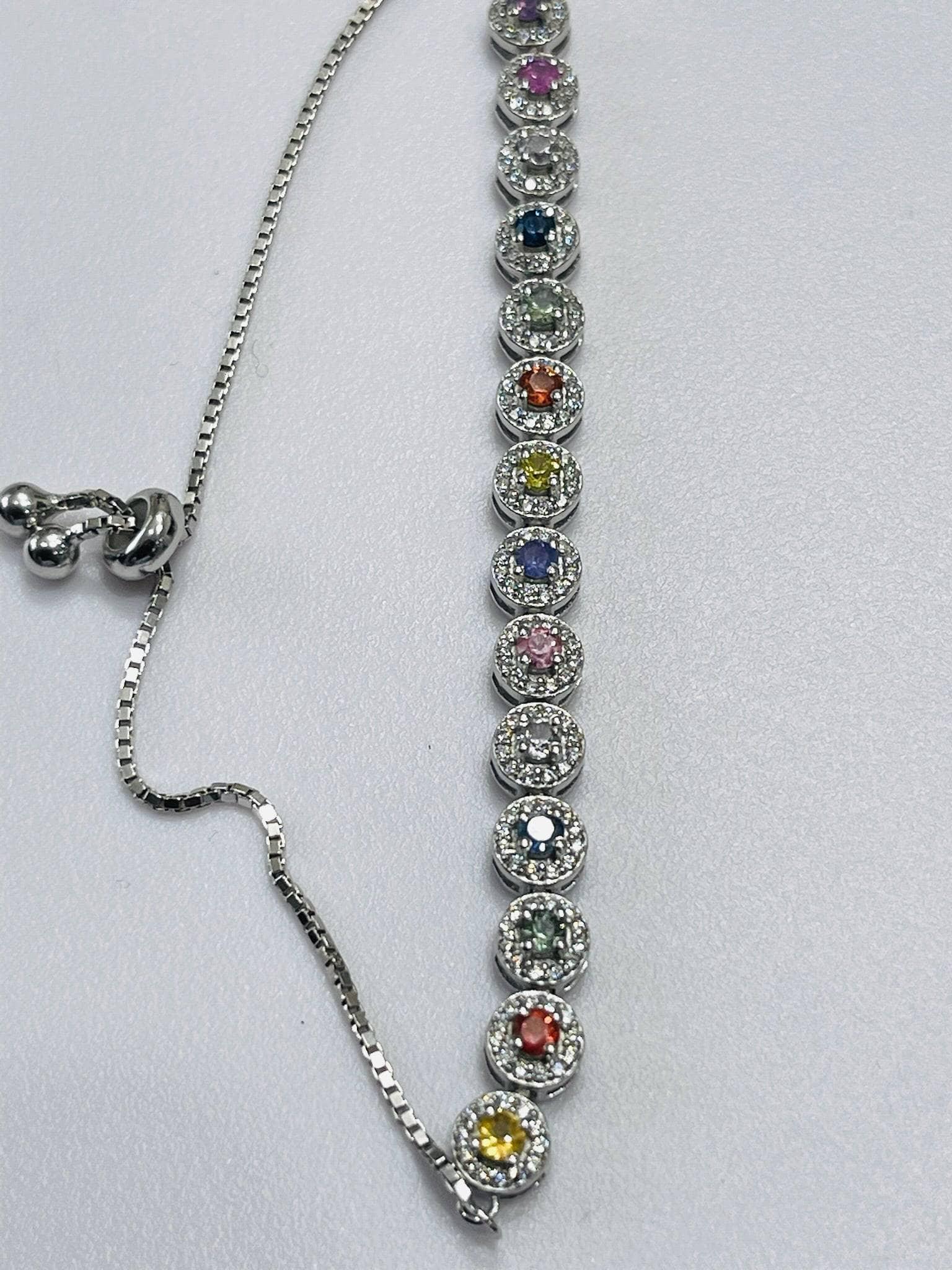  Close-up of a silver bolo bracelet showing multiple round, colorful gemstones in halos, with the adjustable chain.