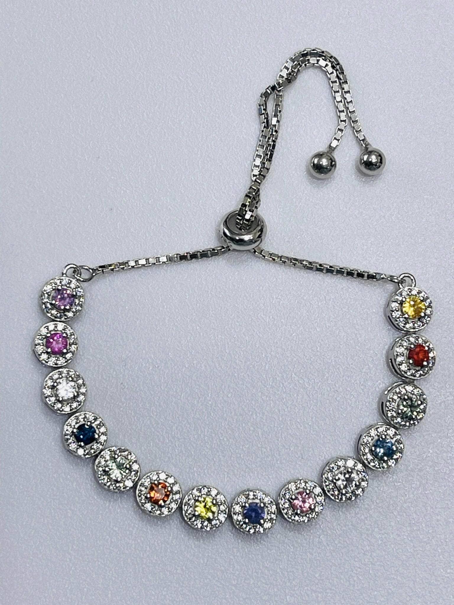 Front view of a silver bolo bracelet featuring a line of round, colorful gemstones each surrounded by small clear stones.