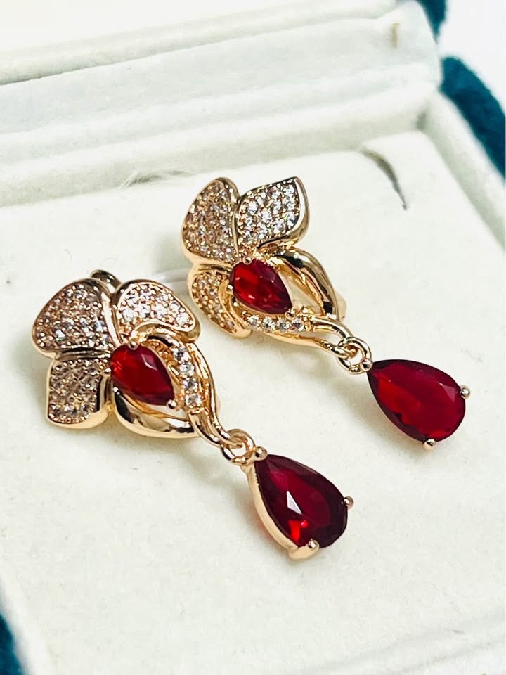 Close-up pair of 14k 585RG stamped red fancy dangle earrings with sparkling clear stones.