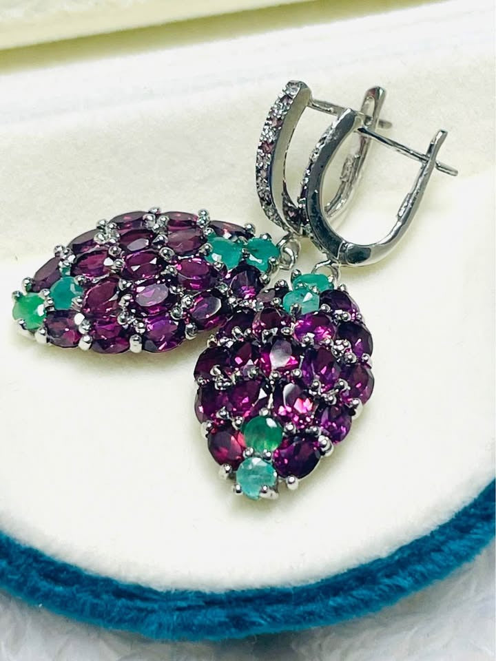 Close-up of exquisite gemstone earrings with rich purple rhodolite garnet and bright green emeralds