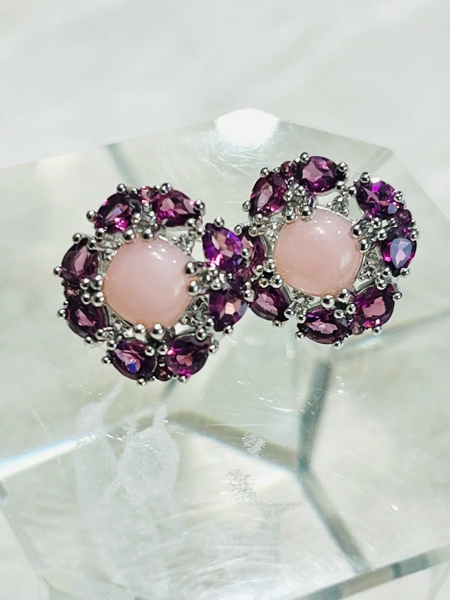 Stylish sterling silver earrings with central pink rose quartz and outer ring of rhodolite garnets, on a clear display.