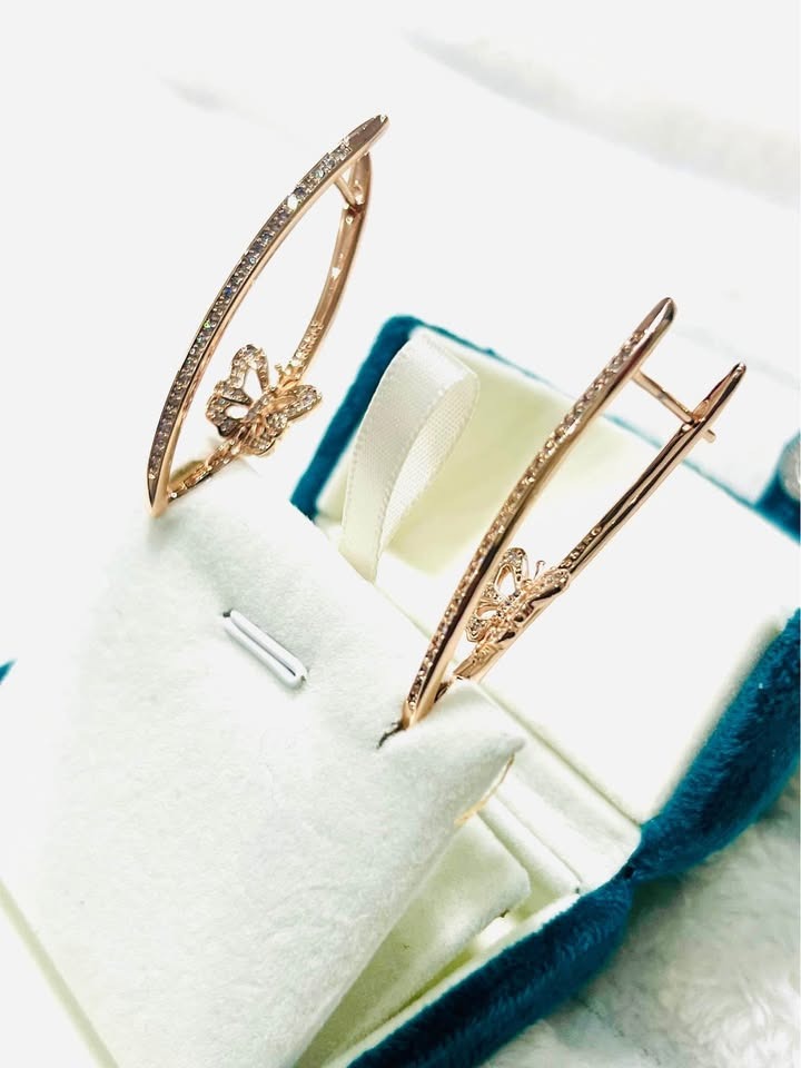 Unique curved rose gold butterfly earrings with sparkling stones, showcased in a blue velvet gift box