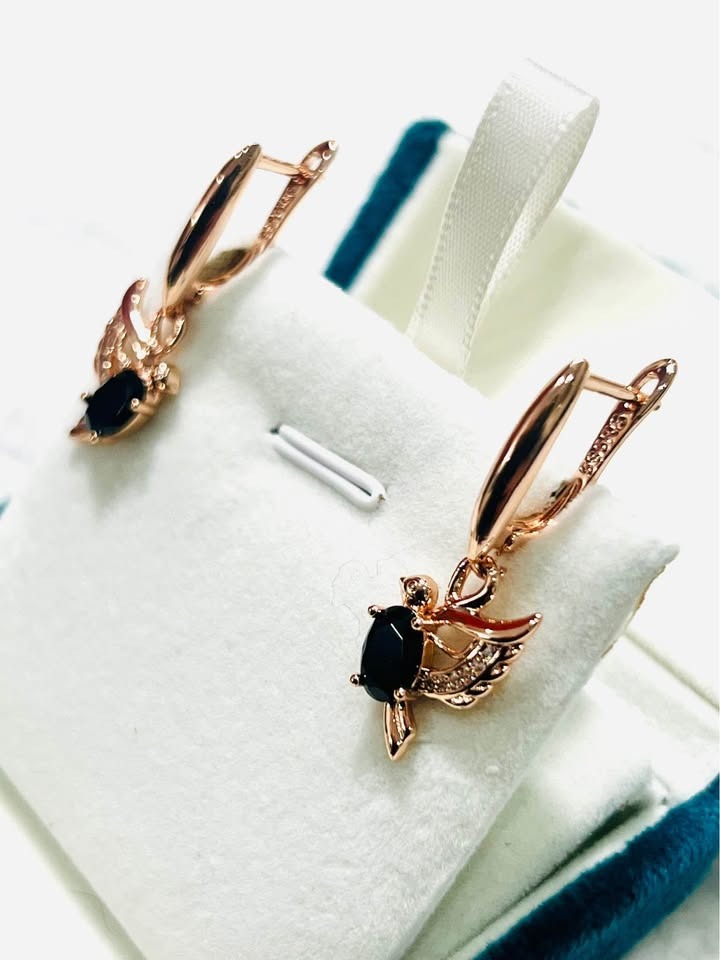 Angled view of 14K gold-filled onyx dove earrings with sparkling accents, displayed in a teal box.